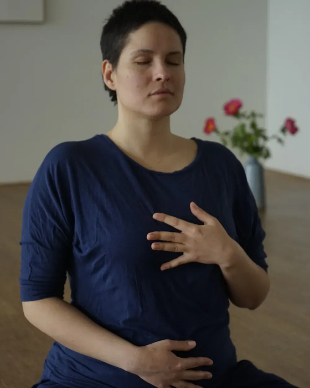 Irene Lähde sitting in a calm restorative pose, eyes closed, one hand resting on the chest and the other on the belly